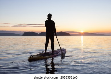 Adventurous Caucasian Adult Woman On A Stand Up Paddle Board Is Paddling On The West Coast Of Pacific Ocean. Sunny Sunrise. Victoria, Vancouver Island, BC, Canada.