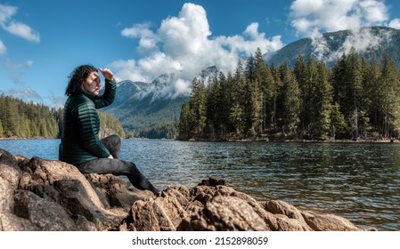 Adventurous Caucasian Woman On The Rocks By The Water In Canadian Nature Landscape. Buntzen Lake, Anmore, Vancouver, BC, Canada. Adventure Travel Concept