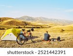 Adventurous cyclist sit by touring bicycle in mountains on side of green tent have break time rest in morning. Solo travel journey. Long-term travel around the world