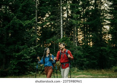 An adventurous and diverse couple eagerly explores a picturesque trail, their backpacks slung over their shoulders, and hiking sticks in hand