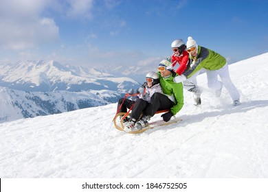 An Adventurous Family Having Fun In The Snow As Father And Son Being Pushed Downhill Through The Snowy Slope While Riding On A Sled