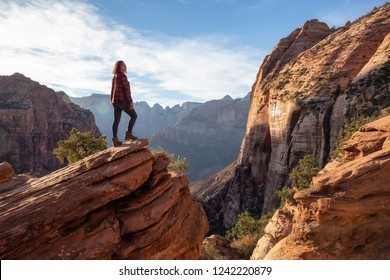 Adventurous Girl at the edge of a cliff is looking at a beautiful landscape view in the Canyon during a vibrant sunset. Taken in Zion National Park, Utah, United States. - Shutterstock ID 1242220879