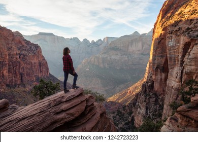 Adventurous Girl at the edge of a cliff is looking at a beautiful landscape view in the Canyon during a vibrant sunset. Taken in Zion National Park, Utah, United States. - Shutterstock ID 1242723223