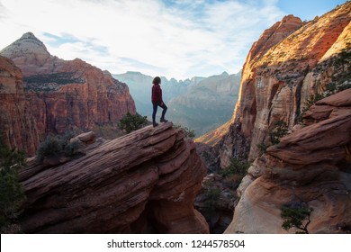 Adventurous Girl at the edge of a cliff is looking at a beautiful landscape view in the Canyon during a vibrant sunset. Taken in Zion National Park, Utah, United States. - Shutterstock ID 1244578504