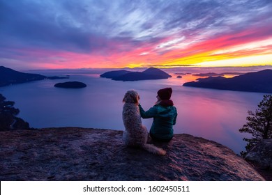 Adventurous Girl Hiking on top of a Mountain with a dog during a colorful sunset. Taken on Tunnel Bluffs Hike, near Vancouver and Squamish, British Columbia, Canada.