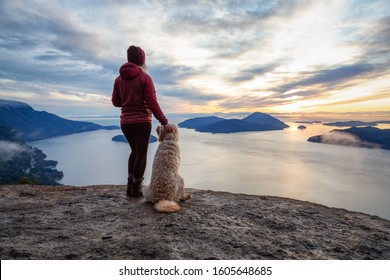 Adventurous Girl Hiking on top of a Mountain with a dog during a colorful sunset. Taken on Tunnel Bluffs Hike, near Vancouver and Squamish, British Columbia, Canada.