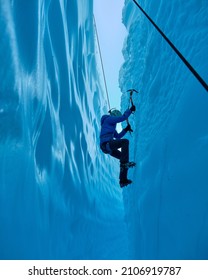 Adventurous Girl Ice Climbing in Slot Canyon Blue Matanuska Glacier in Alaska  Glacier is receding   melting due to global warming  Ice climbing equipment is visible 