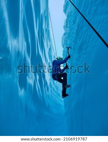 Adventurous Girl Ice Climbing in Slot Canyon on Blue Matanuska Glacier in Alaska. Glacier is receding and melting due to global warming. Ice climbing equipment is visible.