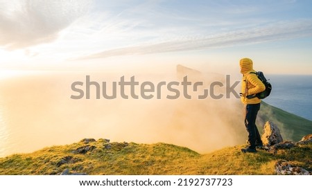 Adventurous man hiker standing on the edge cliff during sunset or sunrise. Travel Lifestyle success motivation concept adventure active vacation outdoors. The boy looks ahead.