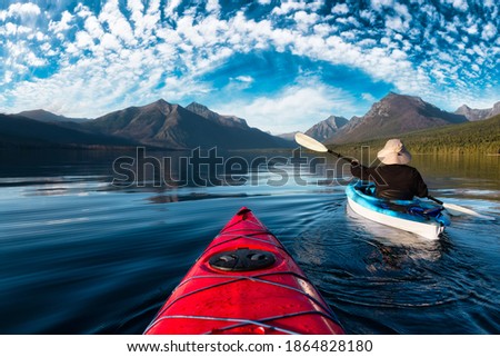 Adventurous Man Kayaking in Lake McDonald during a sunny summer evening with American Rocky Mountains in the background. Taken in Glacier National Park, Montana, USA.