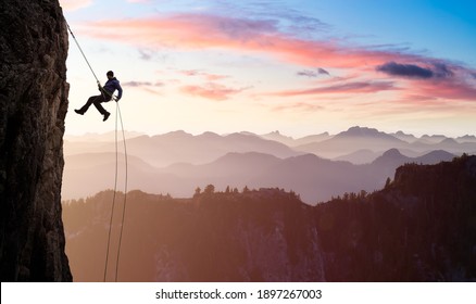 Adventurous Man Rappelling from Cliff. Aerial view of the mountains during a colorful and vibrant sunset or sunrise. Landscape taken in British Columbia, Canada. composite. Concept: Adventure - Shutterstock ID 1897267003