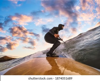 Adventurous Man Surfing the waves at the Pacific Ocean in Tofino, Vancouver Island, British Columbia, Canada. Dramatic Colorful Sunset Sky. Extreme sport