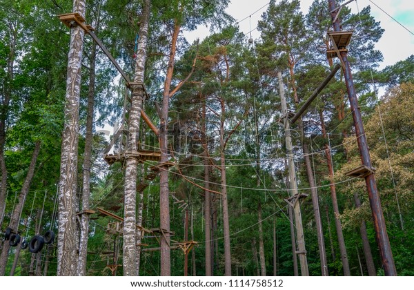Adventurous outdoor activity at an aerial forest\
climbing challenge course, elevated vertigo trekking obstacles with\
bridges, ziplines, climbing, swings, stairs and ladders are\
obstacles to\
traverse