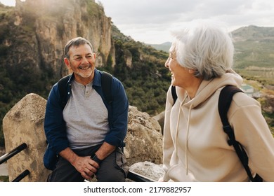 Adventurous Senior Couple Having A Chat While Taking A Break From Hiking. Happy Mature Couple Backpacking In The Hills. Cheerful Elderly Couple Spending Quality Time Together After Retirement.