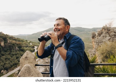 Adventurous senior man using binoculars while standing on a hilltop. Cheerful elderly man enjoying a leisurely hike outdoors. Happy mature man enjoying recreational activities after retirement. - Powered by Shutterstock