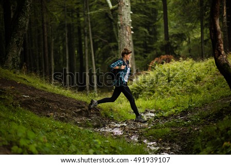 adventurous and sporty woman runs and jumps over a creek in a forest