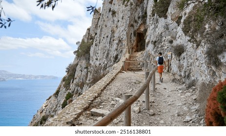 Adventurous Teenage Hiker Explores Dramatic Coastal Cave Entrance Along Scenic Cliffside Trail in Calpe Spain. Intrepid Nineteen-Year-Old Traveler Discovers Hidden Sea Cave Passage Revealing - Powered by Shutterstock