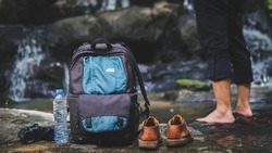 Adventurous Traveler Take Off The Shoes, Drop Their Backpacks And Telescopes To Relax Inside The Waterfall.Concept Of Traveling, Hiking And Relaxing In Nature