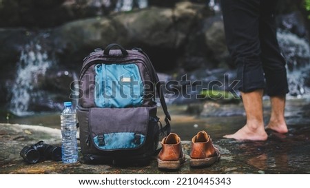 Adventurous traveler take off the shoes, drop their backpacks and telescopes to relax inside the waterfall.Concept of traveling, hiking and relaxing in nature