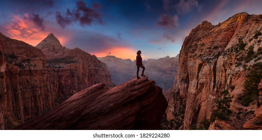 Adventurous Woman at the edge of a cliff is looking at a beautiful landscape view in the Canyon during a vibrant sunset. Taken in Zion National Park, Utah, United States. Sky Composite Panorama - Shutterstock ID 1829224280