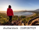 Adventurous Woman Hiker overlooking Sandy Beach on the West Coast of Pacific Ocean. Canadian Nature Landscape Background. Cox Bay Lookout, Tofino, Vancouver Island, BC, Canada.