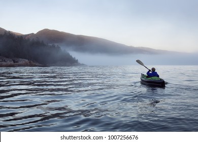 Adventurous woman is sea kayaking on an inflatable kayak during a vibrant winter sunset. Taken in Horseshoe Bay, West Vancouver, BC, Canada. Concept: adventure, holiday, vacation, explore
