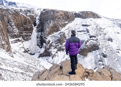 An adventurous young man looking at the frozen Hengifoss waterfall in winter in Iceland - Powered by Shutterstock