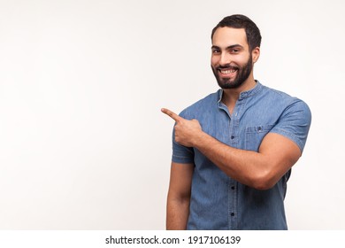Advertise here! Positive bearded man pointing finger away paying your attention at empty space for advertisement, looking at camera with toothy smile. Indoor studio shot isolated on white background