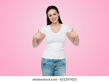 Advertisement, Clothing And People Concept - Happy Smiling Young Woman Or Teenage Girl In White T-shirt Pointing Finger To Herself Over Pink Background
