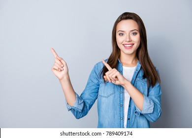 Advertisement concept. Positive, pretty, caucasion woman with beaming smile in jeans shirt  on grey background  is pointing with her two index finger and looking on empty copy space - Powered by Shutterstock