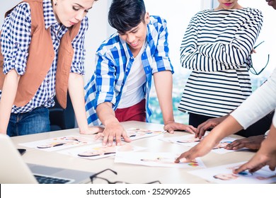 Advertising Agency Team Choosing Model For Campaign Among Pictures Spread Out On Table