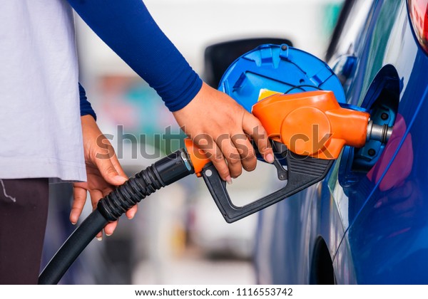 Advertising, Business, Transportation, Technology,\
Energy Concept - Gas station assistant refueling a car. Gas nozzle\
pumping gas into a blue car to fill the machine with fuel at Gas\
station. 