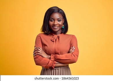 Advertising concept. Confident and smiling young african american woman crossed hands on chest, looking at camera and standing on yellow copy space background.