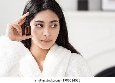 Advertising concept of natural beauty and organic cosmetics. Portrait shot of young asian woman holding bottle with anti wrinkle serum near face, looking aside, standing on copy space white background