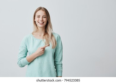 Advertising concept. Smiling cheerful positive european woman wearing light blue shirt pointing her index finger aside at copy space for promotional text, motivating and attracting customers.