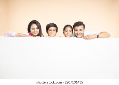 Advertising. Portrait of happy indian family with big white empty banner or poster billboard for content, place for text or image isolated on plane studio background - Powered by Shutterstock