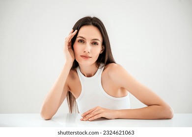 advertising of skincare and bodycare concept. studio shot of young woman with healthy radiant skin looking at camera, hold hand near face, standing isolated against copy paste grey background