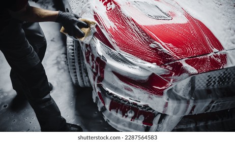 Advertising Style Photo of a Professional Car Wash Specialist Using a Big Soft Sponge to Wash a Beautiful Red Sportscar with Shampoo Before Detailing, Polishing and Waxing