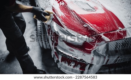 Advertising Style Photo of a Professional Car Wash Specialist Using a Big Soft Sponge to Wash a Beautiful Red Sportscar with Shampoo Before Detailing, Polishing and Waxing