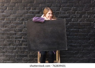 advertisment  emotions  art concept  sitting caucasian woman and long fair haires  she is holding her knees small school blackboard for chalks  there is negative space for text