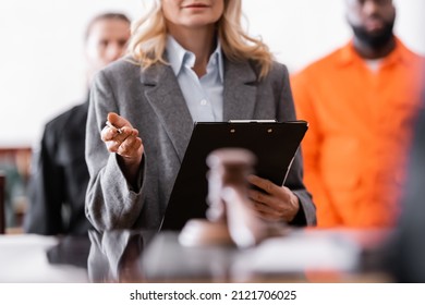 advocate with clipboard standing near accused african american man and bailiff on blurred background