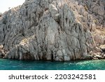 Aegean sea rocky shores with turquoise water. Lava stones and rocks. View from sea. Rock reflection in blue water sea