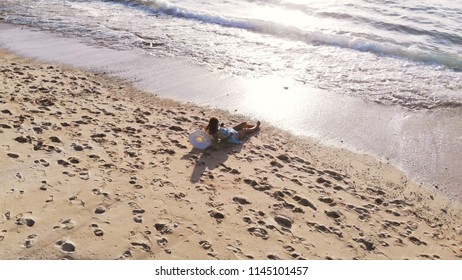 Aereal drone view of young pretty woman is lying on tropical paradise sandy beach and drinks coconut juice during beautiful sunset - Shutterstock ID 1145101457