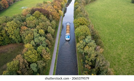 Aerial 4K Bird view shot with a drone of waterway with a barge or freight cargo ship sailing across the natural green orest and farmfield area . High quality 4k footage