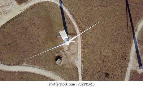 Aerial from above shot of white windmill rotating and producing electricity while placed on terrains of dry desert in sunlight.