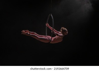 Aerial acrobat in the air ring. Young woman performs the acrobatic elements in the air hoop. Aerialist in on black background dark studio with backlight and smoke. For sports, acrobatic, circus