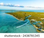 aerial angle of jet ski exiting green lush mangrove channel into blue caribbean sea water during golden hour in turks and caicos islands