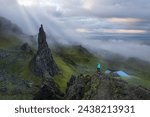 AERIAL: Astounding scene with sunbeams breaking through clouds at Cathedral Rock. Female adventurer is admiring the unique natural attraction and picturesque dramatic landscape on the Isle of Skye.