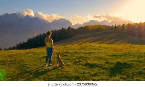 AERIAL: Attractive woman admires view of the mountains on a hilltop with her dog. Amazing sunny autumn day for outdoor recreation in the embrace of picturesque mountains and bonding time with pet. - Powered by Shutterstock