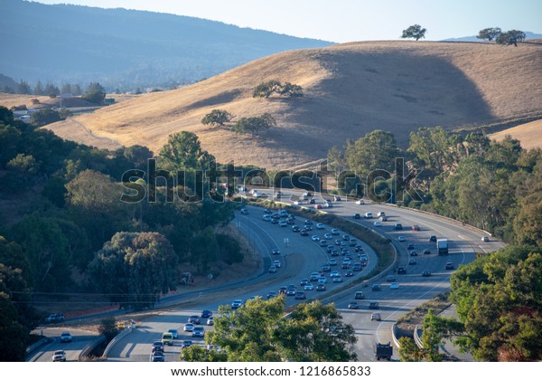Aerial bird\'s eye view of\
heavy evening traffic on curving highway with rolling hill in the\
background